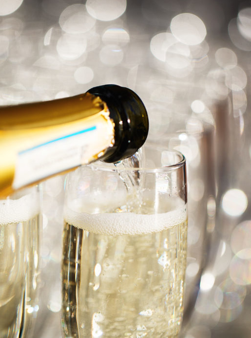 close up of a bottle pouring champagne into glasses with blurred background