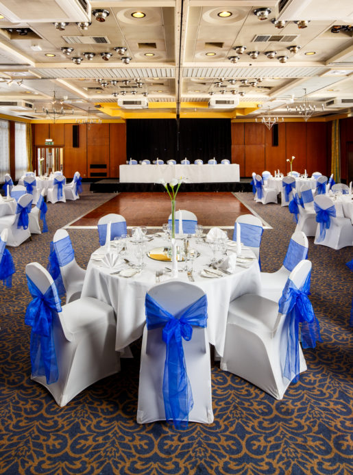 The City Suite at Mercure Norwich Hotel, set up for a wedding breakfast, white linen with blue sashes