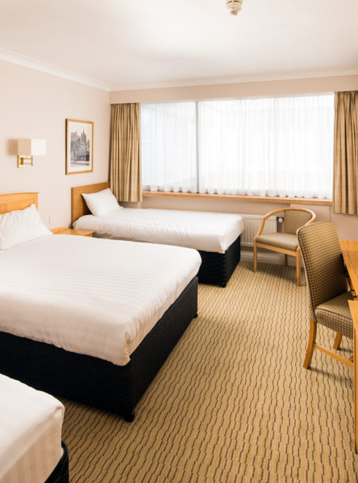 Classic family bedroom at Mercure Norwich Hotel, double bed, two single beds, side table and desk with TV