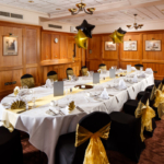 The Club Room at Mercure Norwich Hotel, set up for a wedding breakfast, black and gold theme, star balloons, wood panelling on walls